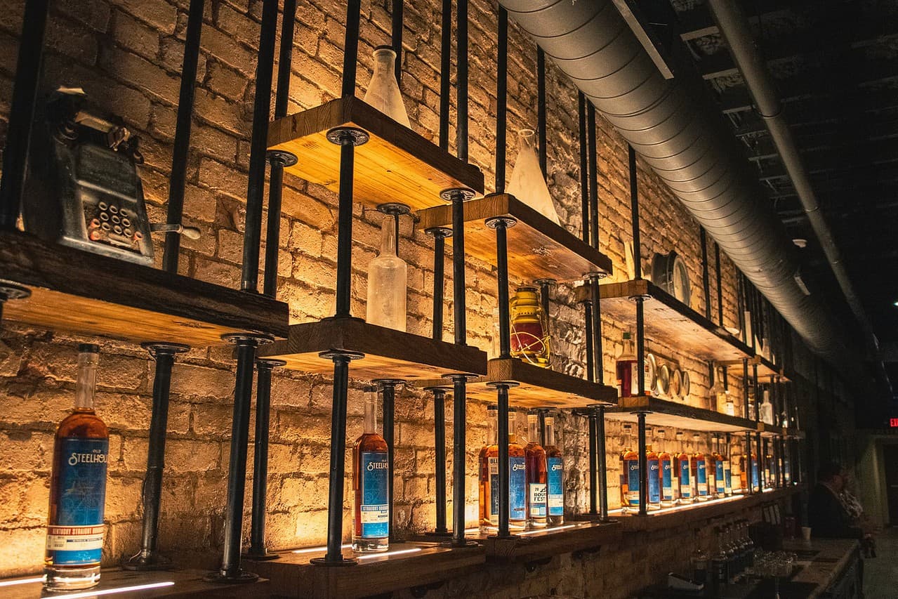Lit shelves of Old SteelHouse bottles against the brick wall of the downtown tasting room